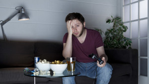 A young man with a sleepy expression playing Sony PlayStation 2 video games on a sofa alongside a table of snacks, taken on July 9, 2013. (Photo by Philip Sowels/Future Publishing via Getty Images)